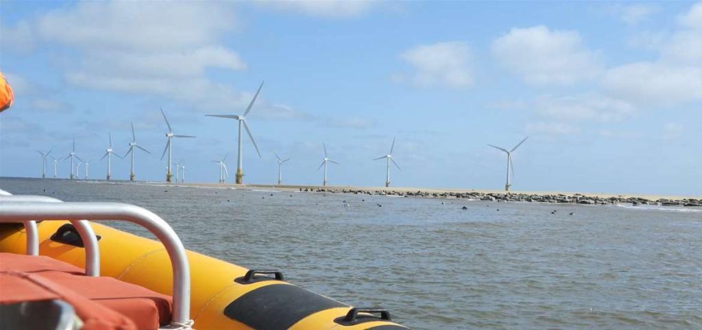 Scroby Sands Wind turbines on seashore behind boat under partly cloudy sky.